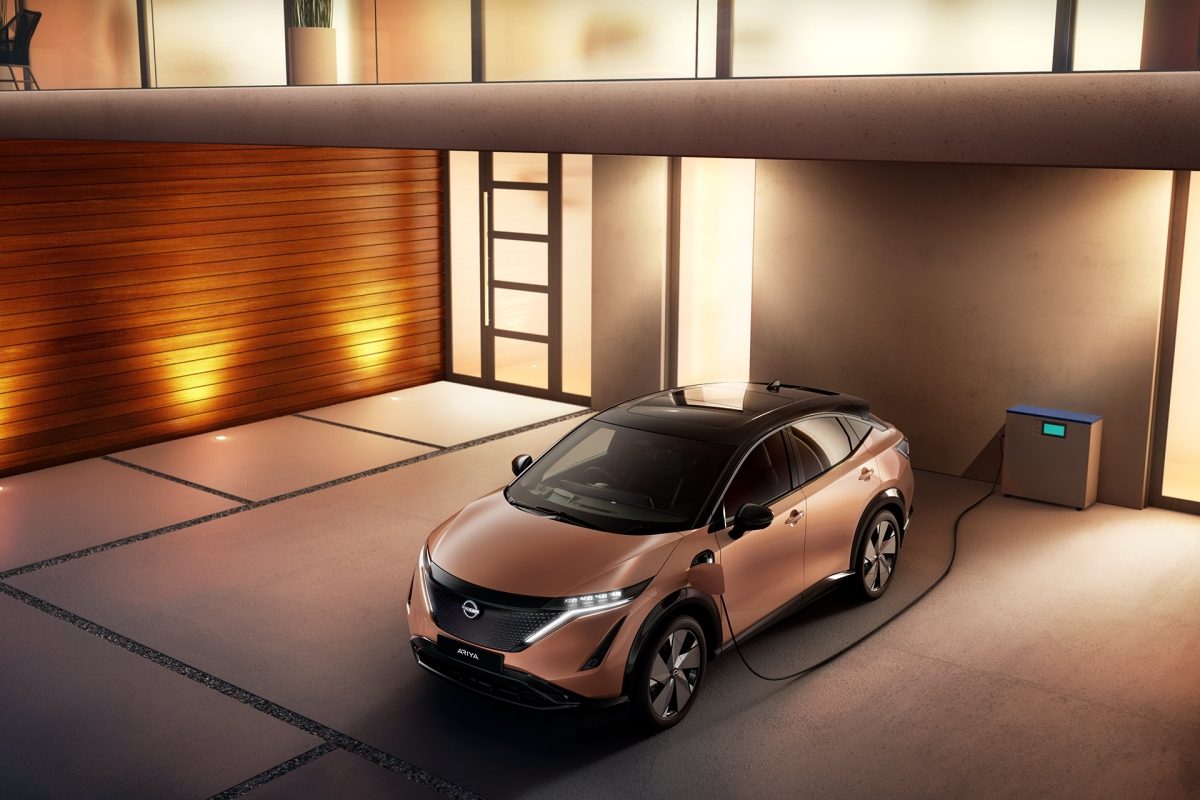 An electric Nissan Ariya plugged into an EV charging point in a spacious modern garage.
