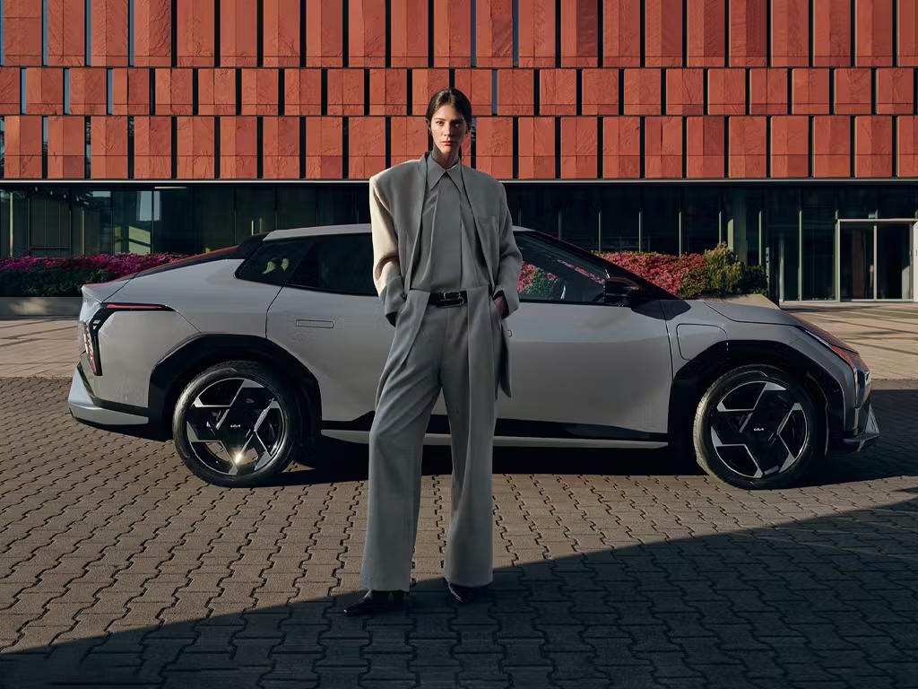 Side profile of the Kia EV4 in pearl white, featuring bold angular alloy wheels, a sleek fastback silhouette and distinctive LED lighting against a contemporary urban backdrop.