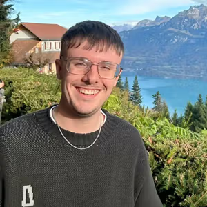 Outdoor portrait of a person standing in front of a scenic mountain and lakeside view.