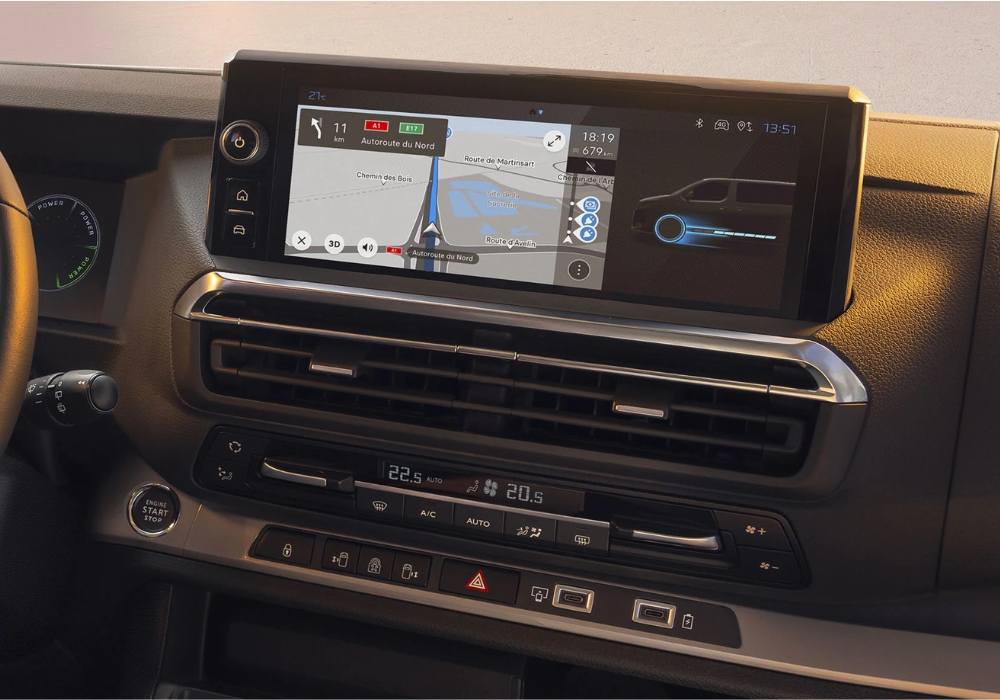 Close-up of Peugeot E-Traveller infotainment screen displaying navigation and vehicle information above dashboard controls.