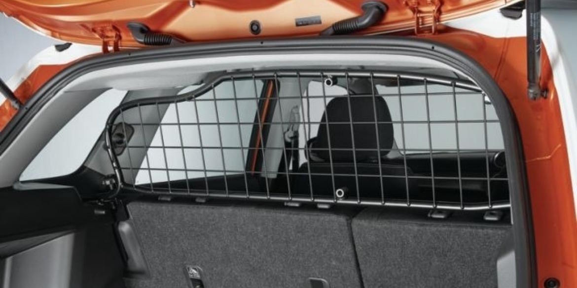 Boot space view of an orange Suzuki SUV fitted with a sturdy black metal dog guard, separating the cargo area from the rear passenger seats.