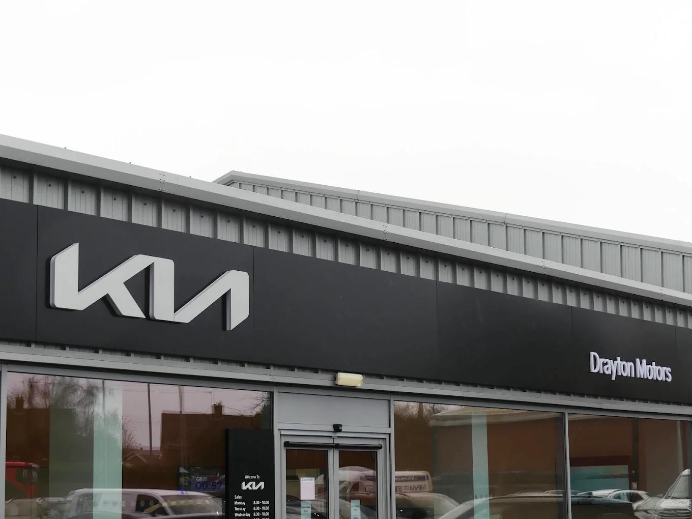 Exterior view of Drayton Motors Kia dealership in Louth, featuring the modern Kia logo and brand signage on the sleek dark grey façade with large glass showroom windows