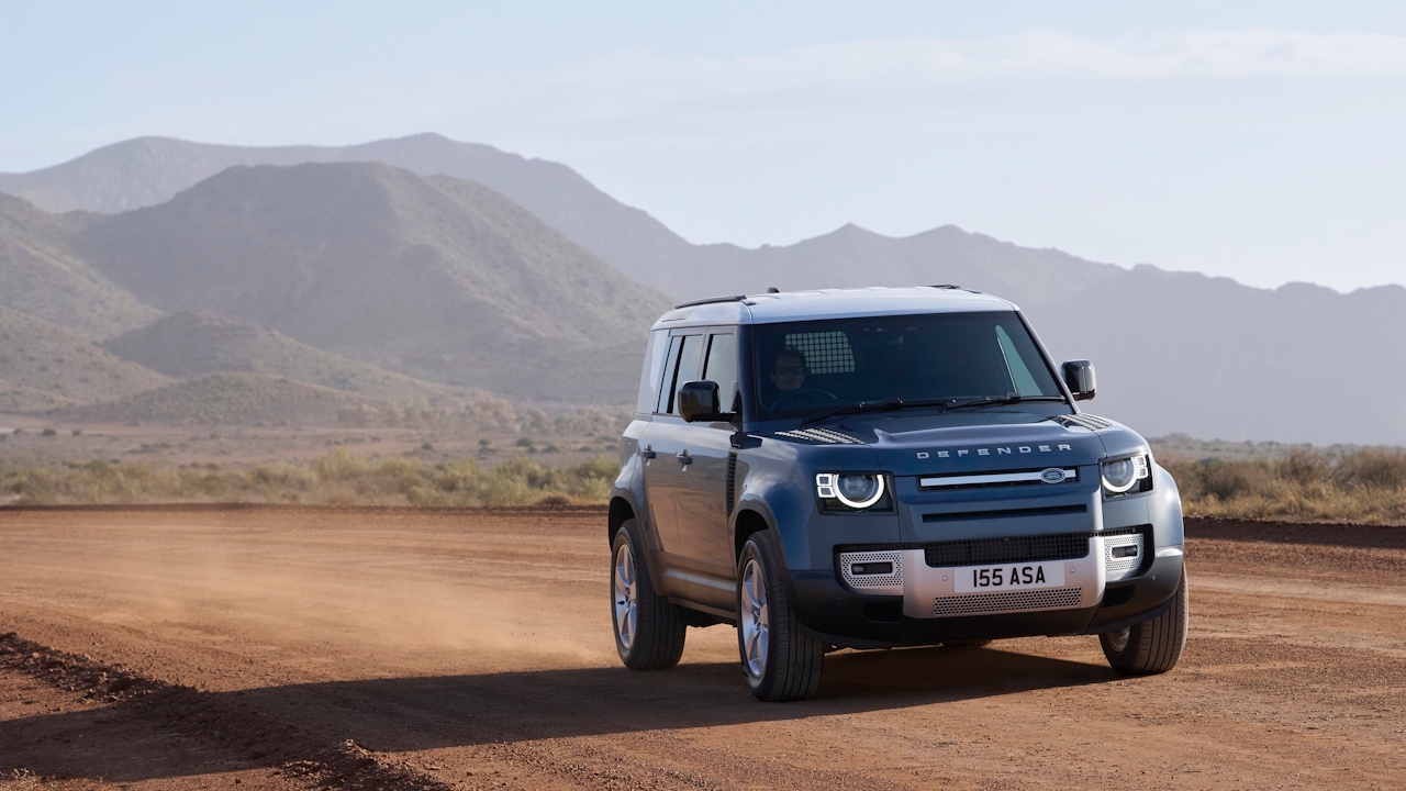 Front three-quarter view of the Defender Hard Top driving on a dusty dirt road in a desert landscape.