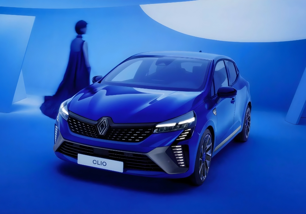 Blue Renault Clio hatchback in a studio setting with a person walking in the background.