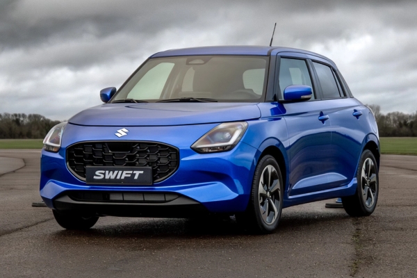 Blue Suzuki Swift parked outdoors on an overcast day in a front three-quarter view.
