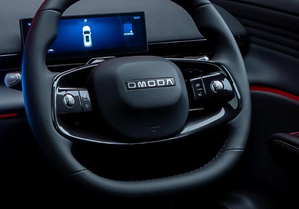 Close-up of OMODA steering wheel with integrated controls and a digital driver display screen behind it.