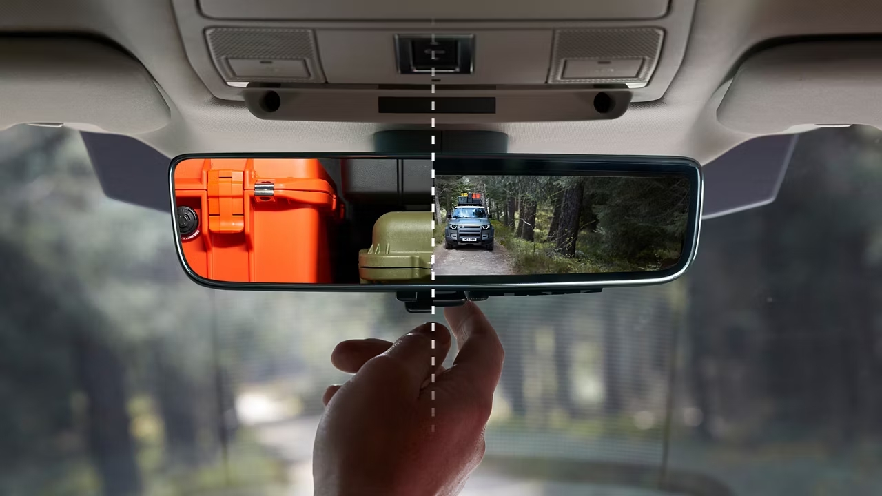Digital rear-view mirror display showing a vehicle driving on a forest track behind.