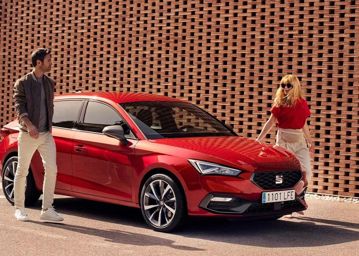 Red SEAT Leon with a man and woman beside it
