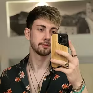Portrait of a person wearing a floral shirt and jewellery while taking a mirror photograph.