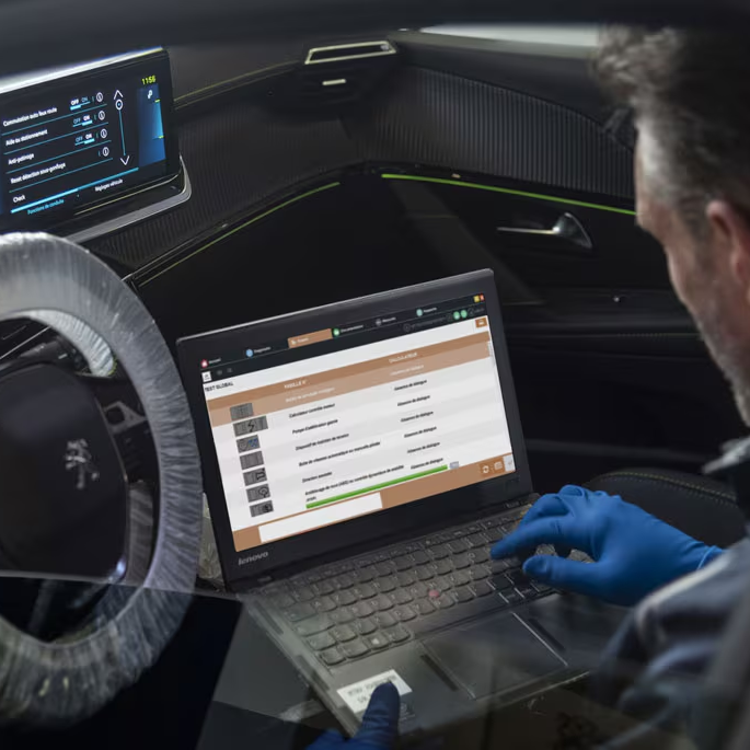 Technician using a laptop inside a vehicle to run diagnostics, with the infotainment screen and dashboard visible.