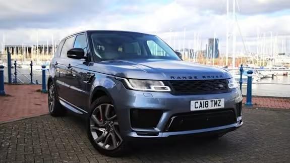 Silver Range Rover Sport SUV parked on a harbourside with boats and masts in the background, viewed from the front three‑quarter angle.